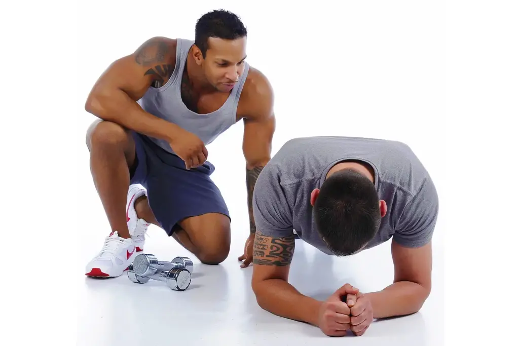 Personal trainer coaching a client doing a forearm plank exercise.