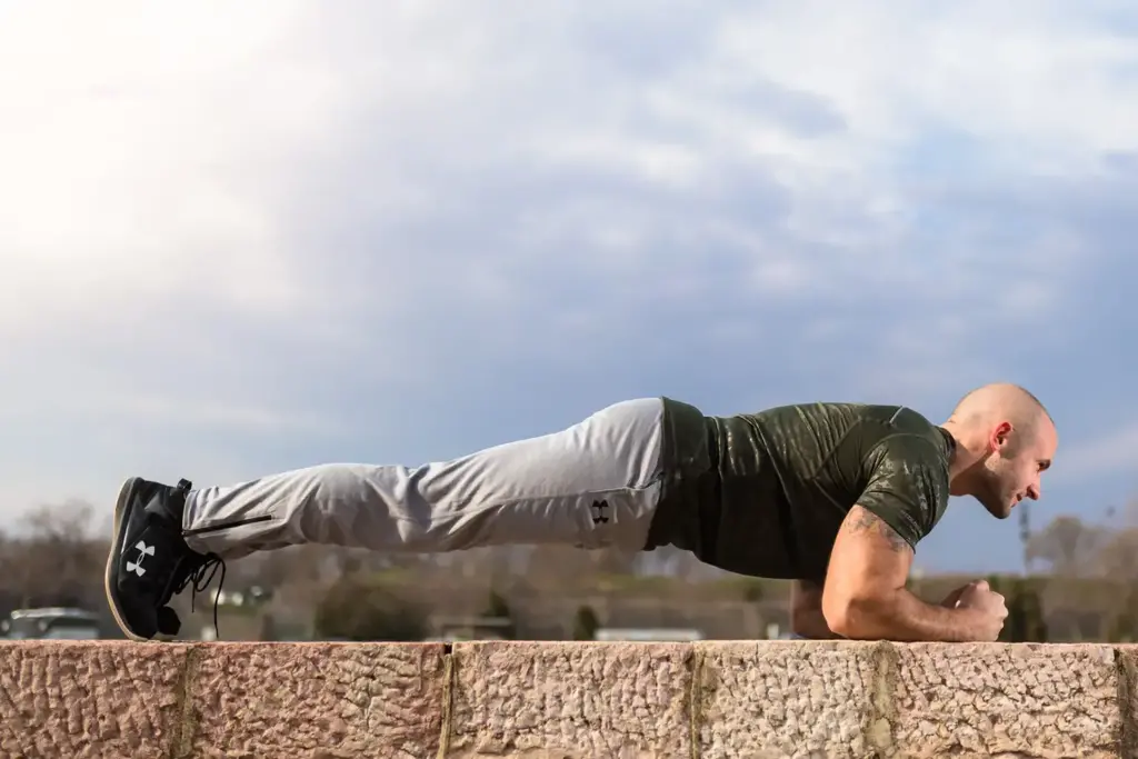 Man holding a plank position on a stone wall outdoors.